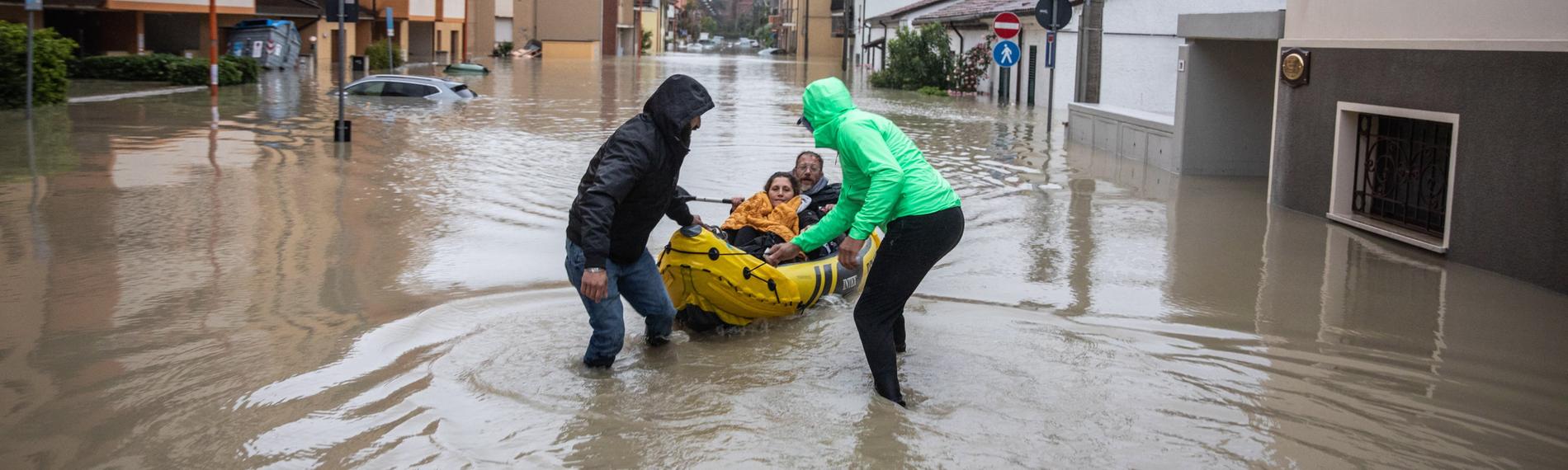 Zwei Männer ziehen Schlauchboot hinter sich her bei Hochwasser in Norditalien