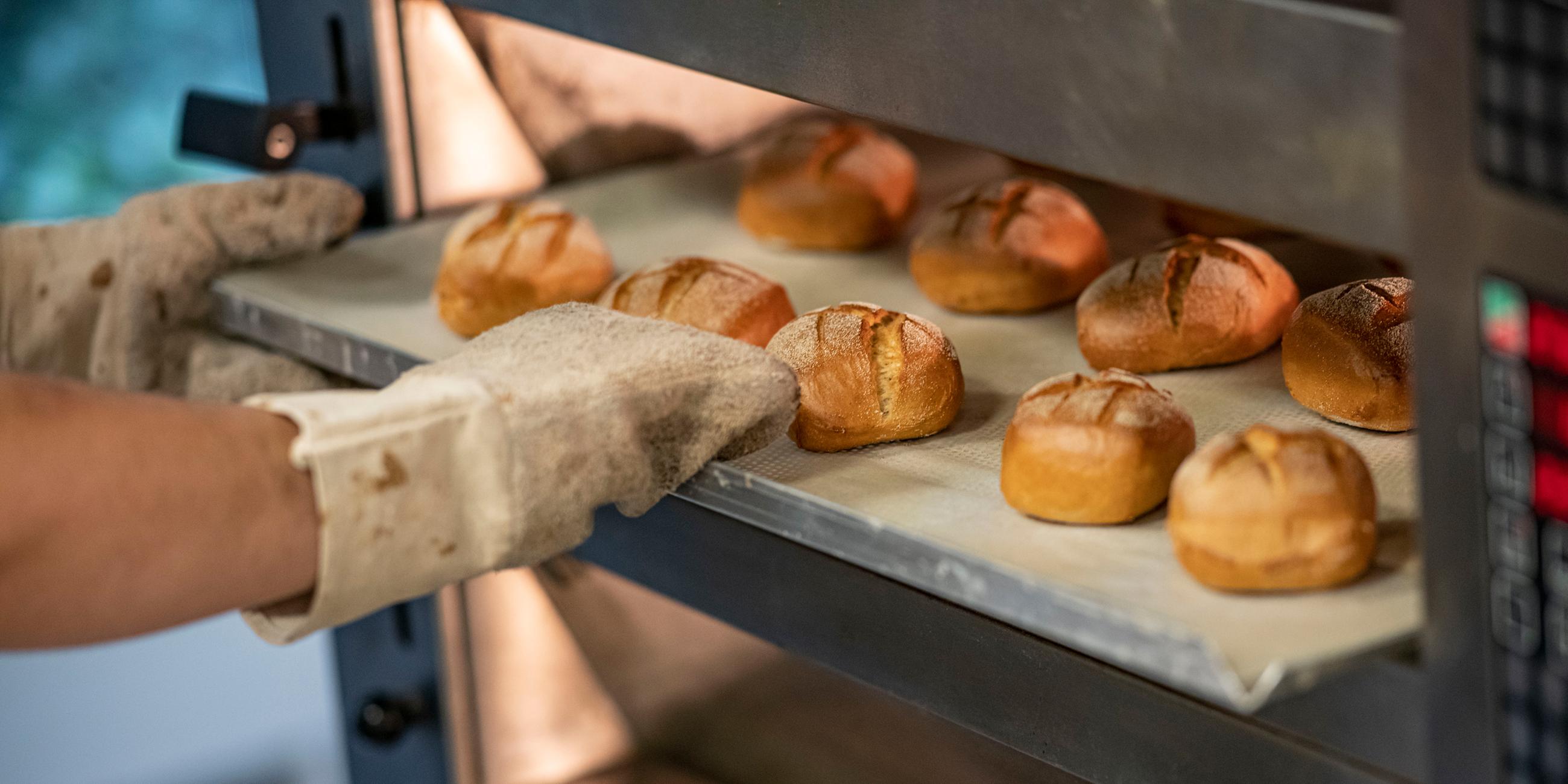 Ein Bäcker schiebt ein Blech mit Brötchen in den Ofen.