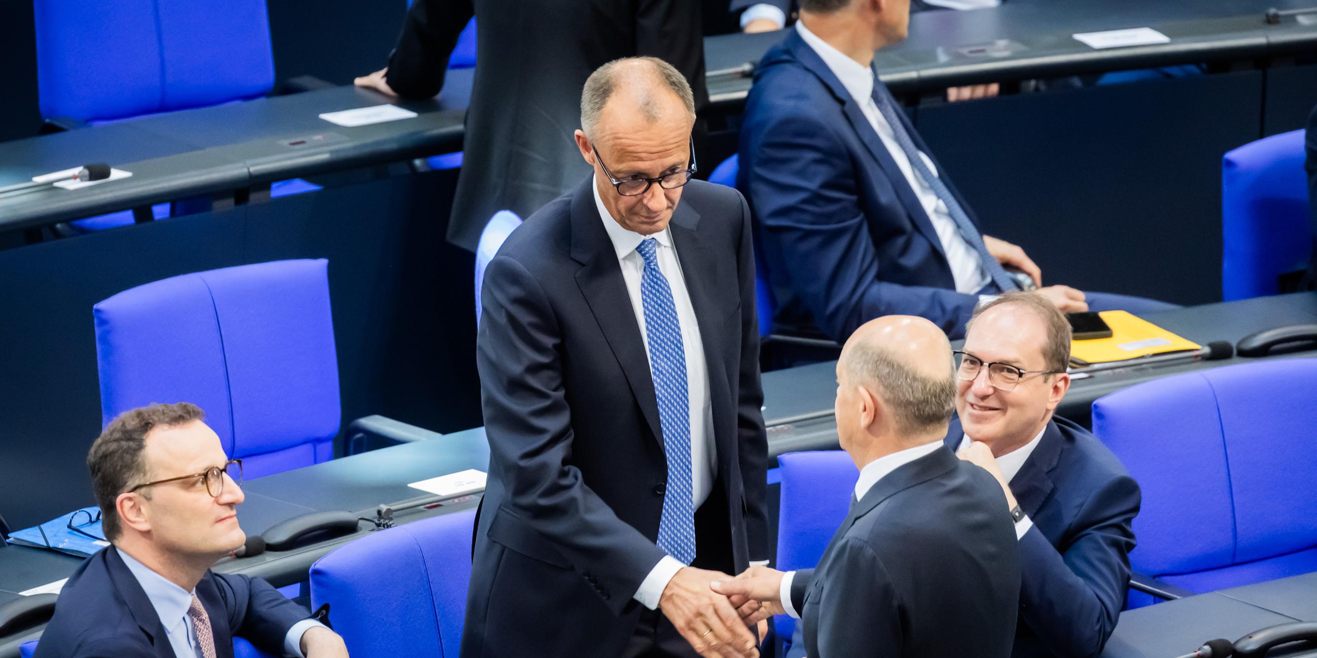 Berlin: Der designierte Bundeskanzler Friedrich Merz (CDU, M oben) und der geschäftsführende Bundeskanzler Olaf Scholz (SPD, unten M) schütteln sich neben Jens Spahn (CDU, l), Vorsitzender der CDU/CSU Bundestagsfraktion, und Alexander Dobrindt (CSU, r), designierter Innenminister, im Bundestag beim zweiten Durchgang der Kanzlerwahl die Hand.