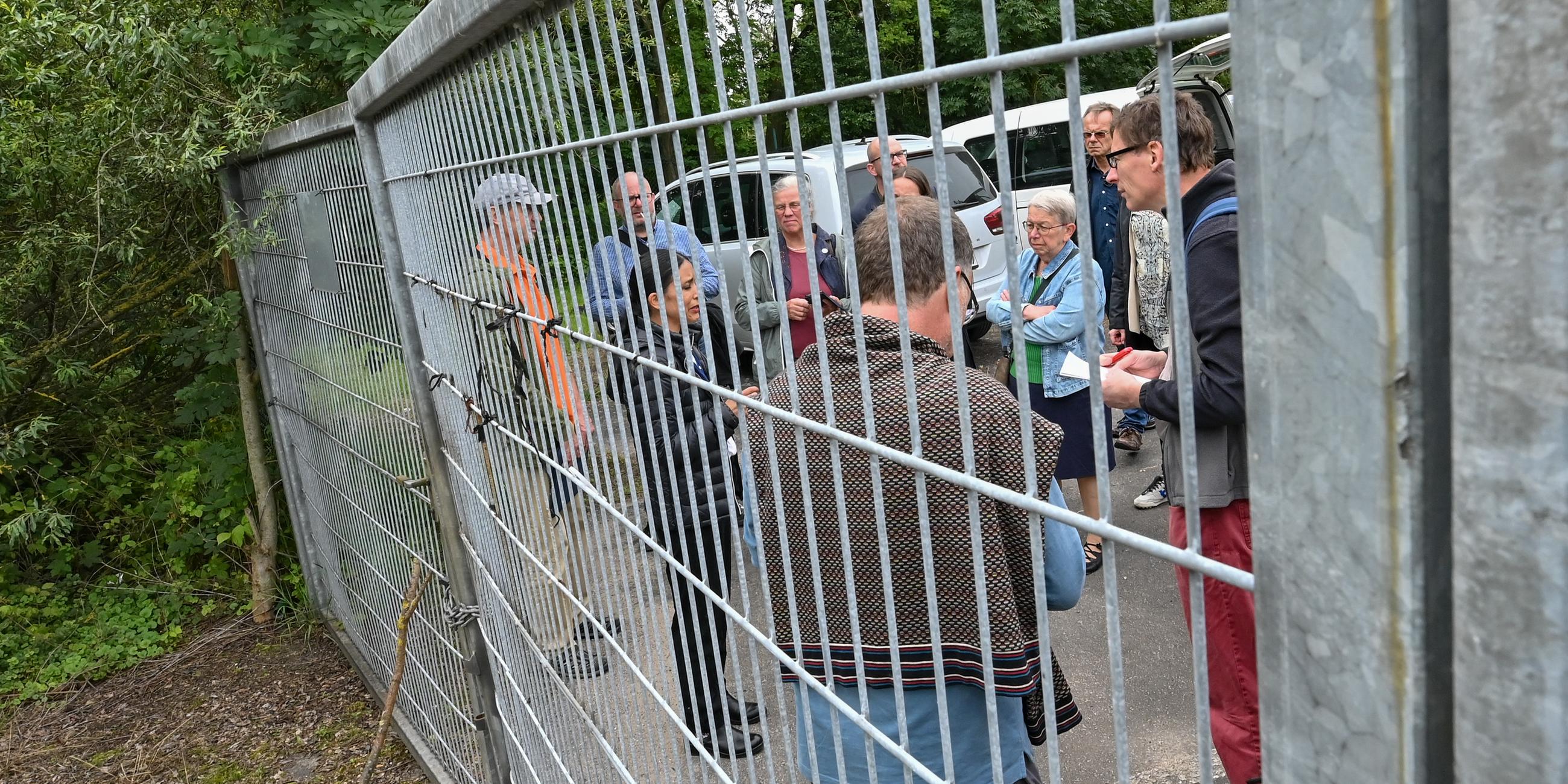 Diana Gonzalez Olivo, Landesintegrationsbeauftragte Brandenburg und Wolfgang Henschel, künftiger Ortsvorsteher von Küstrin-Kietz, stehen vor einem verschlossenem Tor zu einem Gelände mit alten Kasernenanlagen.