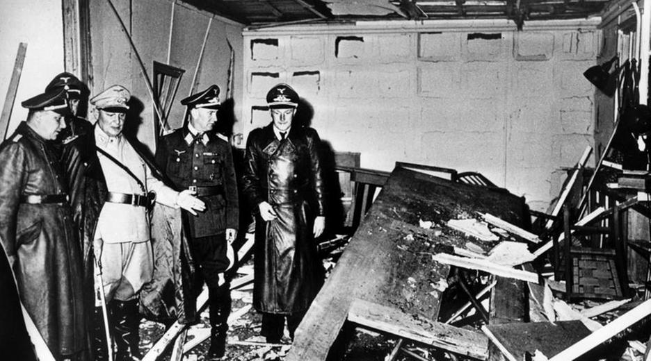 Schwarz-weiß Foto vor den Überresten des Hitler-Attentats 1944. Menschen stehen vor den Trümmern.