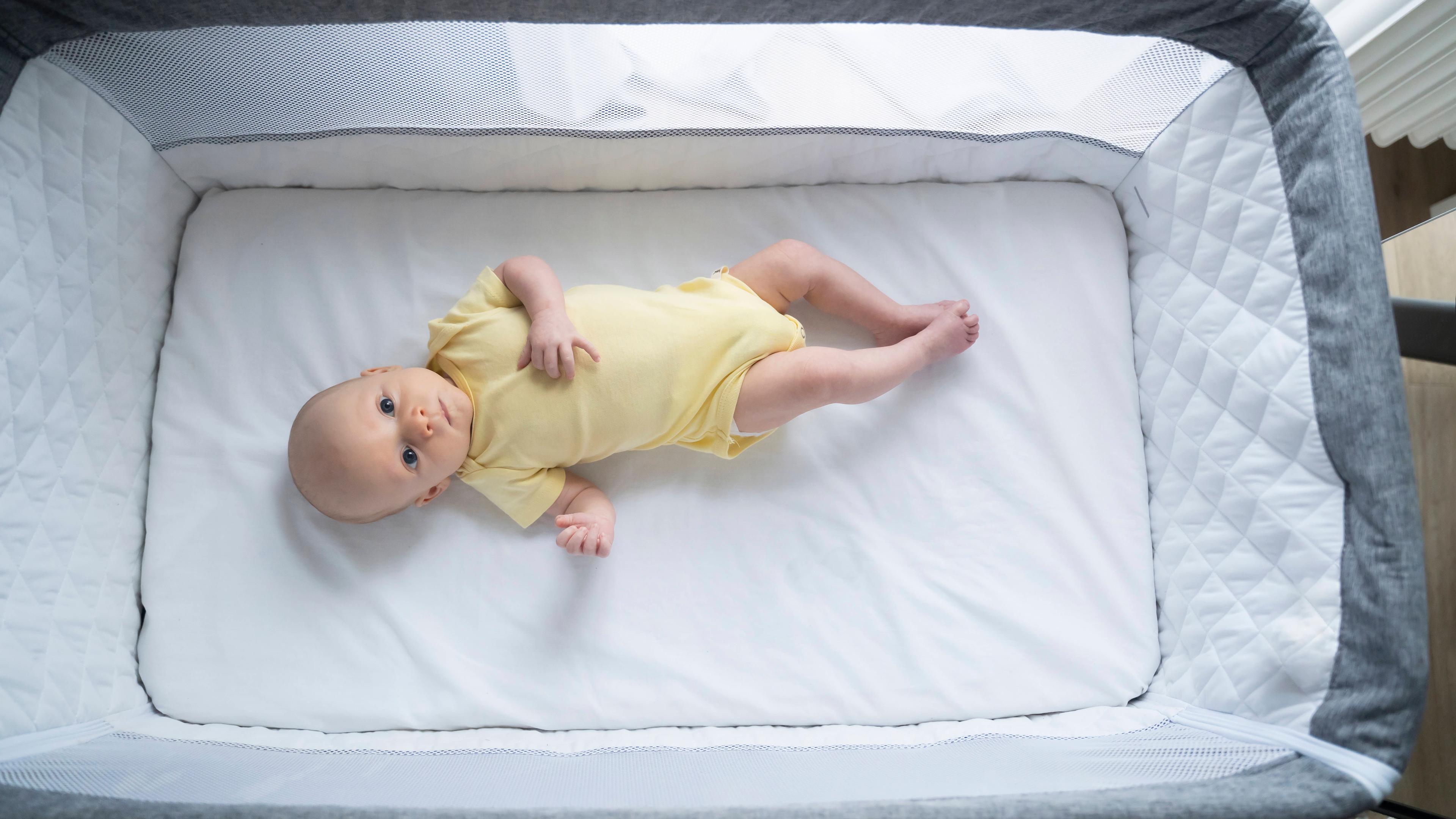 Ein Baby liegt auf dem Rücken in einem Babybett.