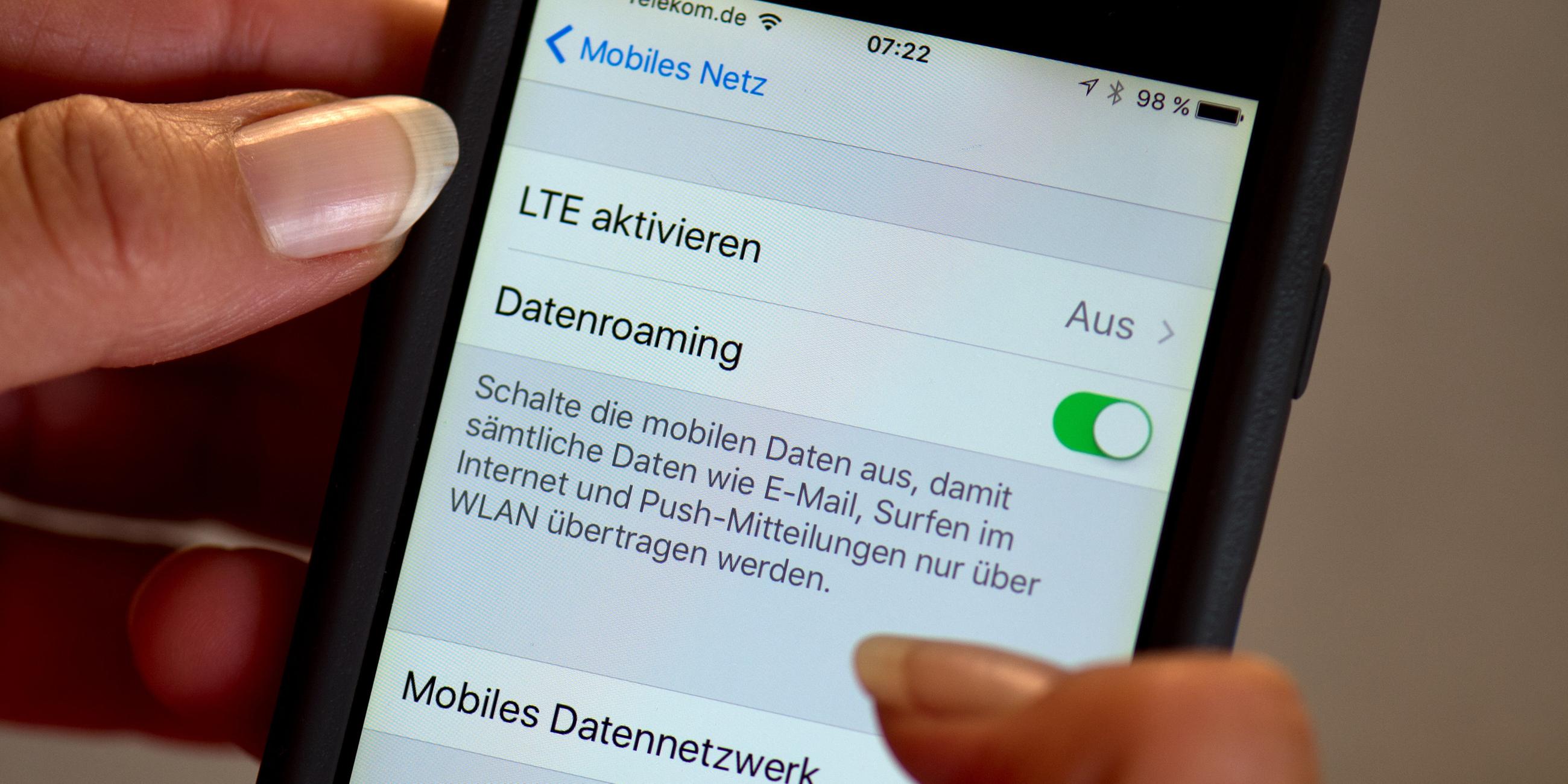 Eine Hand hält ein Smartphone. Darauf sind die Einstellungen für das Datenroaming und mobile Daten zu sehen.