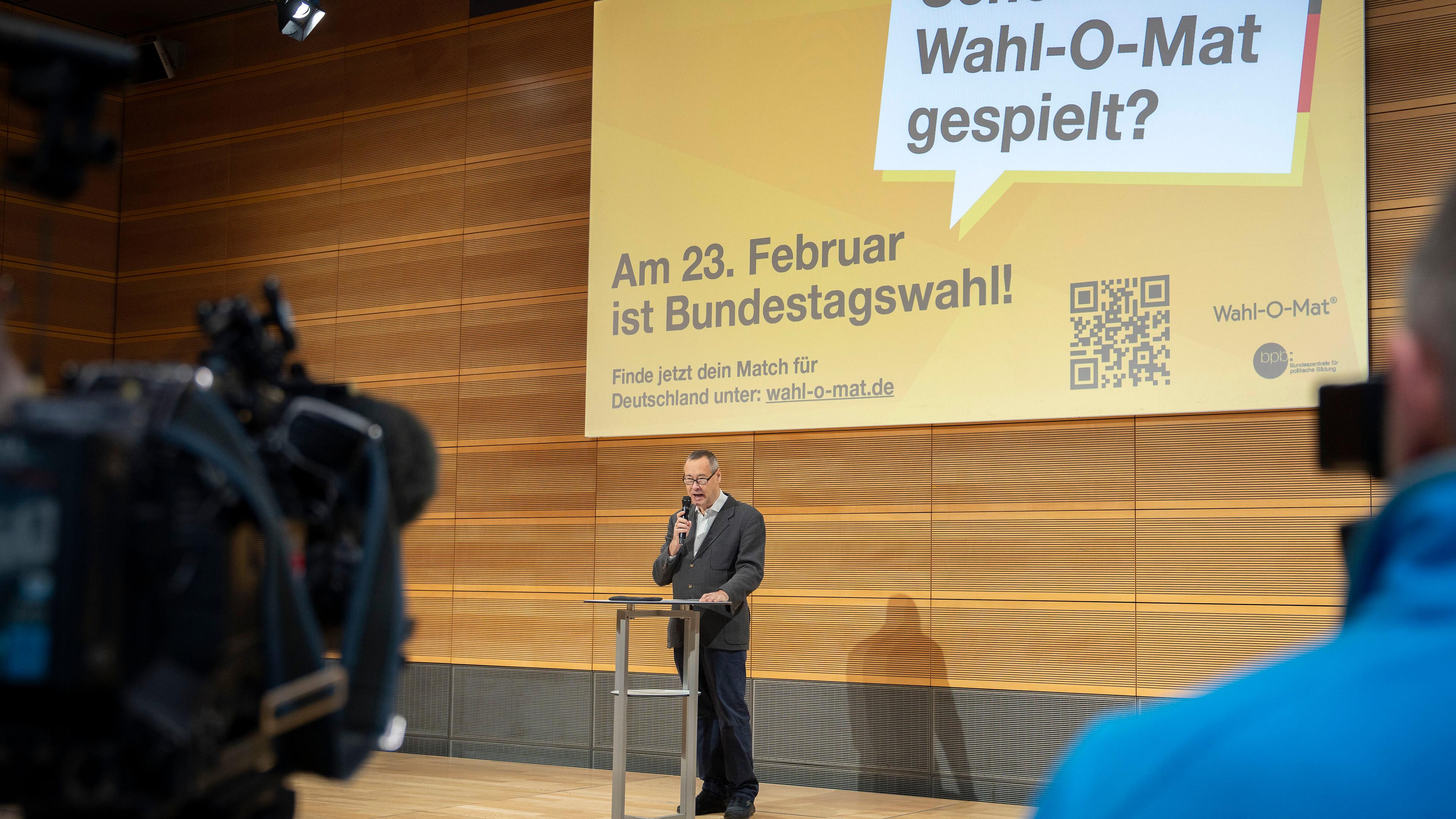 Ein Mann steht auf einer Bühne. Im Hintergrund ist eine Leinwand mit dem Hinweis auf den Wahl-O-Mat zu sehen.