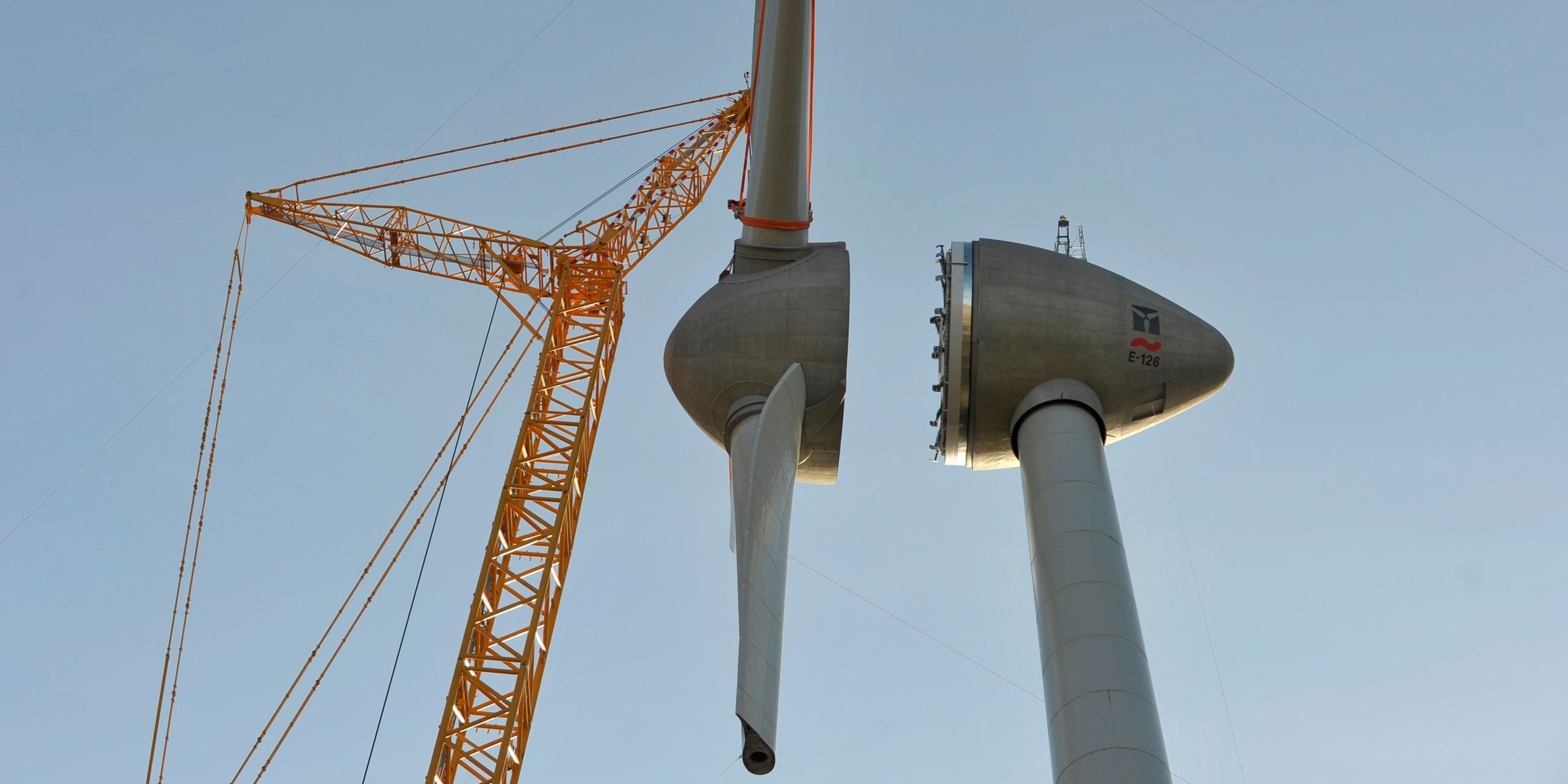 Die Rotorblätter werden mit Hilfe eines Krahns an eine Windkraftanlage gebaut